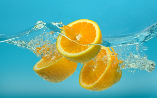 Naranjas cayendo en agua con salpicaduras sobre fondo azul turquesa