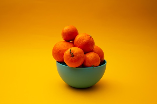 Naranjas cítricas en un recipiente sobre un fondo amarillo