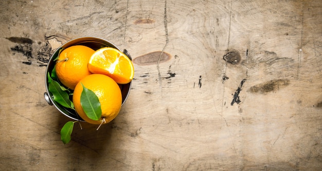 Naranjas en un cubo de hojas. Sobre fondo de madera.