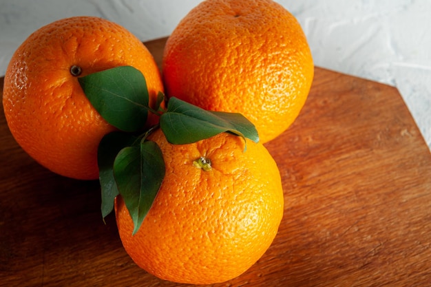 Naranjas enteras sobre una tabla de madera sobre un fondo blanco con vista superior de hojas verdes