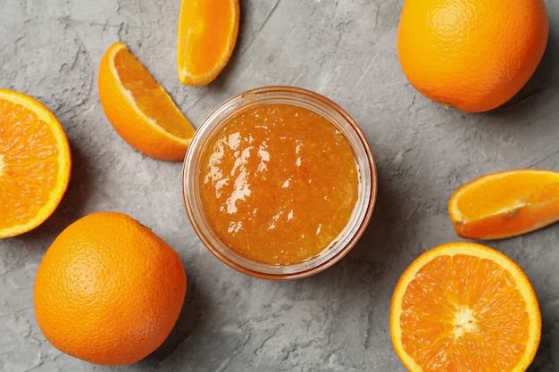 Naranjas y frasco de vidrio con mermelada sobre fondo gris, vista superior