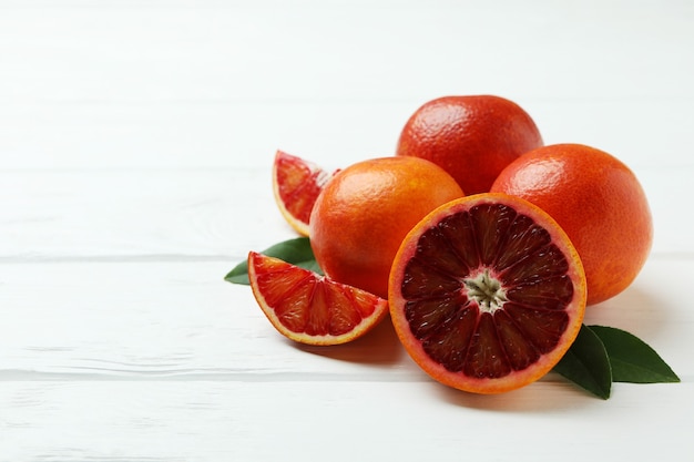 Naranjas rojas y hojas en la mesa de madera blanca, espacio para texto