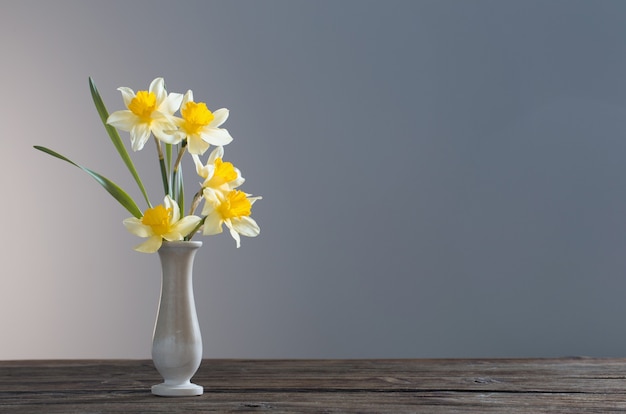 Narciso amarelo em um vaso na mesa de madeira em fundo escuro