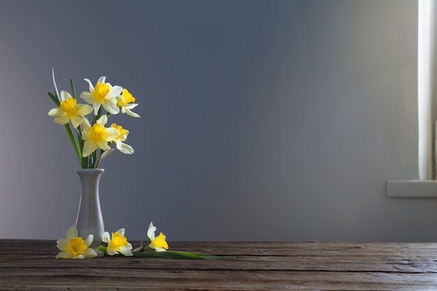 Narciso amarelo em um vaso na mesa de madeira na superfície escura