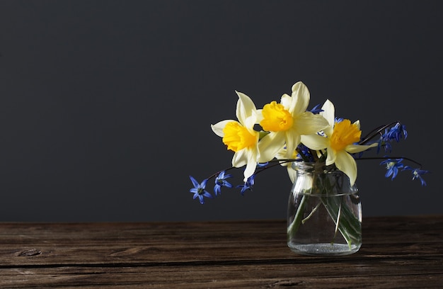 Narciso amarillo y campanillas azules en un jarrón sobre la mesa de madera sobre fondo oscuro