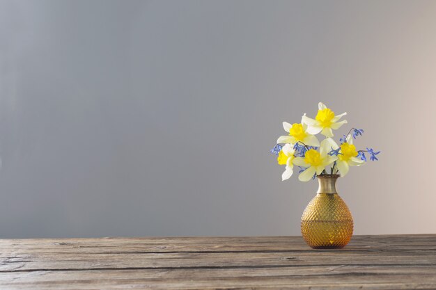 Narciso amarillo y campanillas azules en un jarrón sobre la mesa de madera sobre la superficie gris