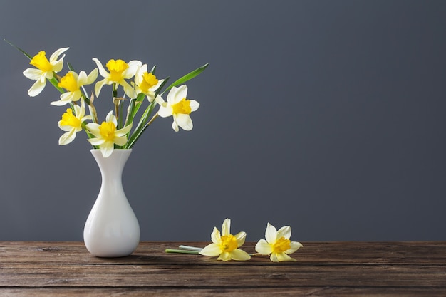 Narciso amarillo en un jarrón sobre la mesa de madera sobre fondo oscuro