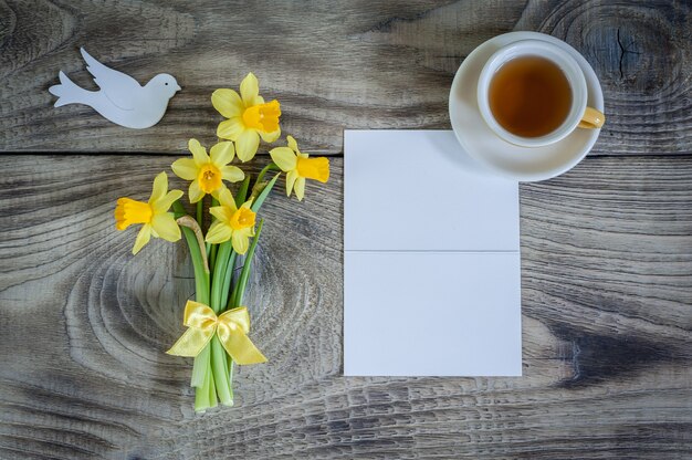 Narcisos amarelos com cartão, pássaro e copo do chá no fundo de madeira. Feliz Dia das Mães,