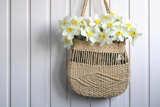 Foto narcisos en una bolsa de mimbre en una pared de tablero blanco en un colgante de fondo floral de verano