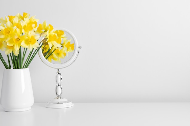Narcisos de flores amarillas en jarrón y reflejo de flores en el espejo