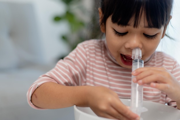 La nariz de lavado nasal de solución salina de niña asiática en casa