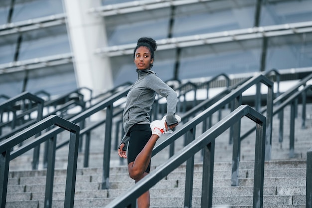Nas escadas A jovem afro-americana em roupas esportivas faz exercícios ao ar livre durante o dia