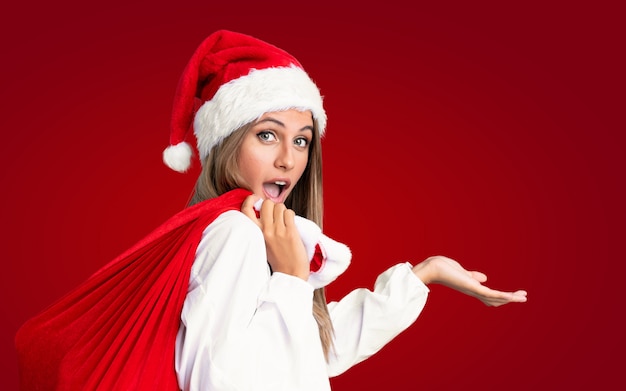 Nas férias de natal Jovem mulher loira pegando um saco cheio de presentes ao longo da parede vermelha isolada