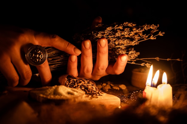 Foto nas mãos das bruxas, ramo de ervas secas para adivinhação. a luz das velas na velha mesa mágica. atributos de ocultismo e magia.