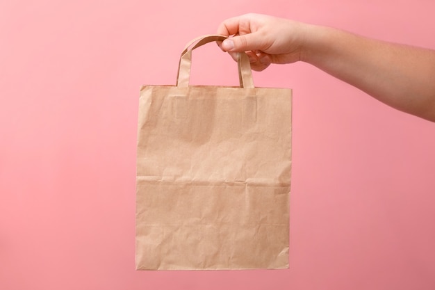 Nas mãos de um saco de papel de mulher em fundo rosa