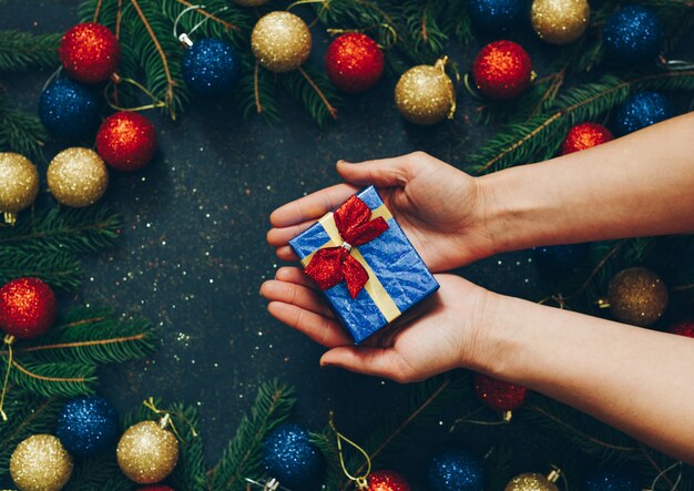 Nas mãos de uma menina segurando um presente em um fundo preto com brinquedos de natal