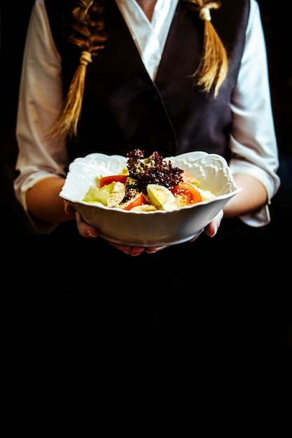 Nas mãos do garçom sobre um prato está uma salada de legumes frescos