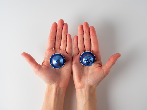 Nas mãos dos homens estão duas cápsulas de café de alumínio azul. Uma das cápsulas é usada