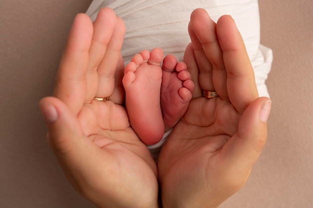 Nas palmas das mãos do pai, a mãe segura o pé do bebê recém-nascido em uma manta branca. Pés do recém-nascido nas palmas dos pais. Fotografia de estúdio dos dedos dos pés, calcanhares e pés de uma criança.