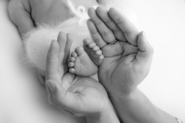 Nas palmas das mãos do pai, a mãe segura o pé do bebê recém-nascido. Pés do recém-nascido nas palmas dos pais. Fotografia de estúdio dos dedos dos pés, calcanhares e pés de uma criança. Preto e branco.