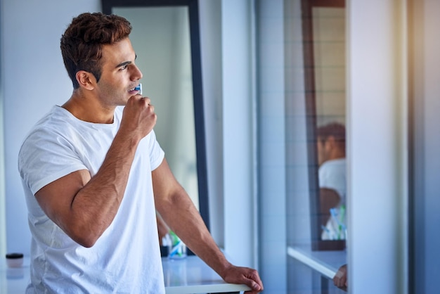 Nas profundezas da zona de rotina matinal Foto de um jovem bonito olhando pensativo enquanto escova os dentes em casa