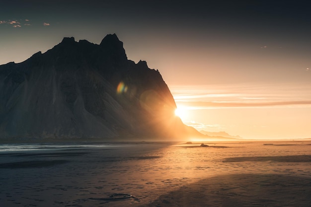 Nascer do sol dourado na montanha vestrahorn pelo oceano atlântico e praia de areia preta na península de stokksnes islândia