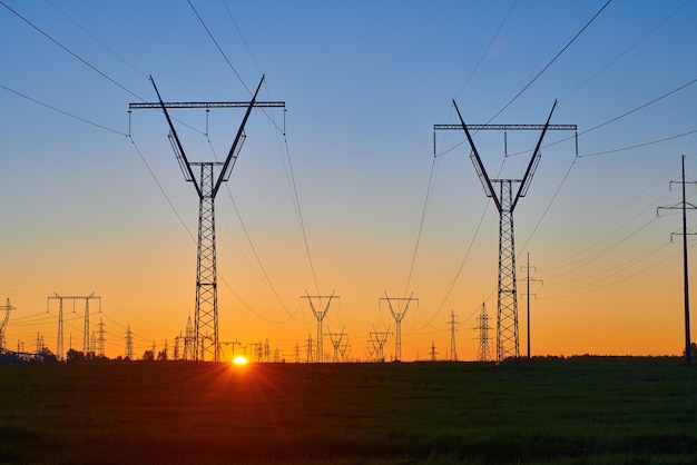 Nascer do sol laranja em campo com torres de eletricidade de alta tensão silhuetas escuras de linhas de energia repetidas no nascer do sol rede de transmissão e distribuição de geração de eletricidade paisagem industrial