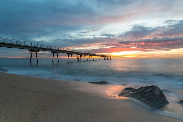 Nascer do sol na praia com uma ponte no final sob um céu colorido