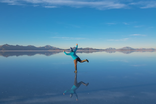 Nascer do sol no Salar de Uyuni na Bolívia coberto de água, turista mulher no deserto plano salgado e reflexões do céu