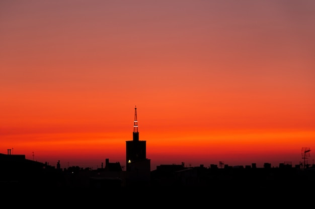 Nascer do sol vermelho roxo do verão, vista superior do telhado de uma torre de igreja velha acima da cidade.