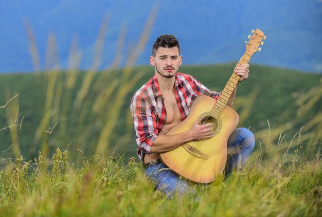 Nascido para balançar moda hipster ocidental camping e caminhadas homem vaqueiro feliz e livre com guitarrista acústico música country música homem sexy com guitarra em camisa quadriculada