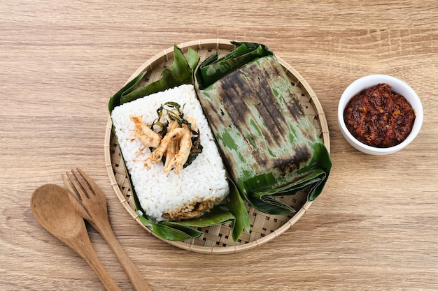 Nasi Bakar-Reis mit Gewürzen, eingewickelt in Bananenblätter, mit würzigem Hähnchenschnitzel und Basilikumblättern