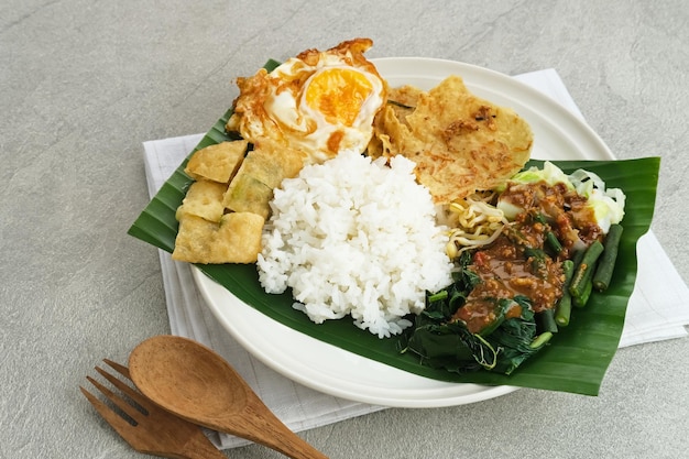 Nasi Pecel, un arroz javanés tradicional con ensalada de verduras y salsa de maní, servido con guarnición