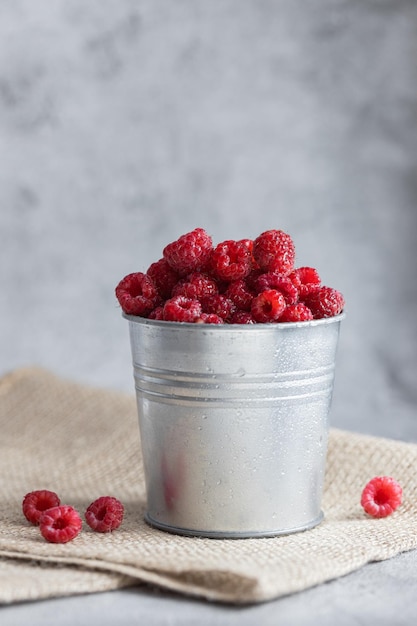 Nasse Himbeeren in einem Metalleimer auf einem grauen Hintergrundfoto Essen Sommerfruchtzusammensetzung