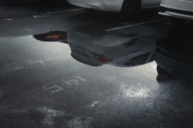 Nasse Parkplätze nach starkem Regen fallen mit Reflexion des Autos in Pfütze auf dem Boden. Selektiver Fokus.