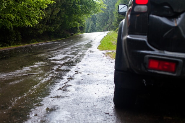 Nasse Straße nach Regen und Auto am Straßenrand im Wald