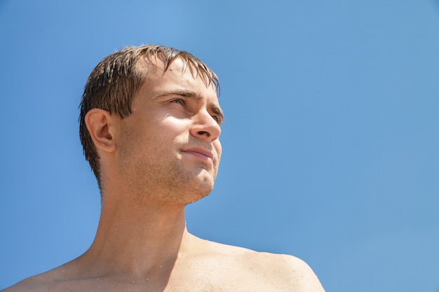 Nasser junger Mann auf blauem Himmel