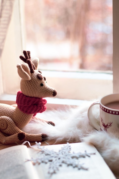 natal ainda vida. xícara de café, livro aberto, cobertor branco, veado de Natal de brinquedo perto da janela de luz