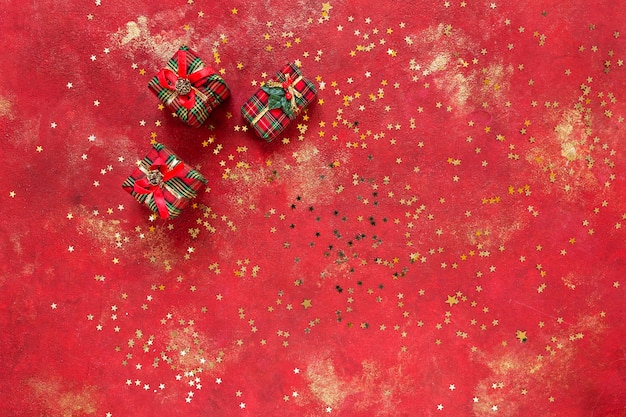 Natal, caixas de presente de ano novo em fundo vermelho e dourado festivo com confete em forma de estrela de glitter dourado. Vista de cima, close-up