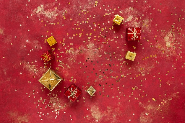 Natal, caixas de presente de ano novo em fundo vermelho e dourado festivo com confete em forma de estrela de glitter dourado. Vista de cima, close-up