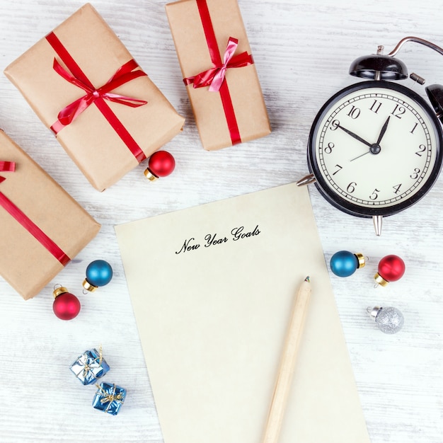 Natal com caixas de presente, despertador, bolas de decoração de Natal e folha de papel na mesa de madeira branca