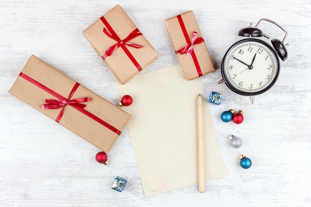 Natal com caixas de presente, despertador, bolas de decoração de natal e folha de papel na mesa de madeira branca