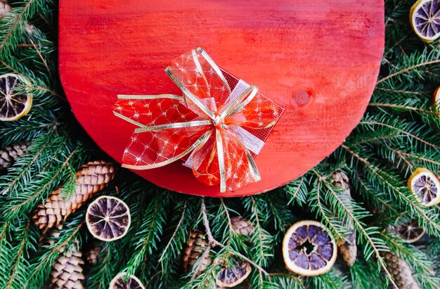 Natal, composição de férias de inverno de ano novo com superfície de madeira vermelha em galhos de árvore verde do abeto, fatias de laranja secas, cones e laço vermelho.