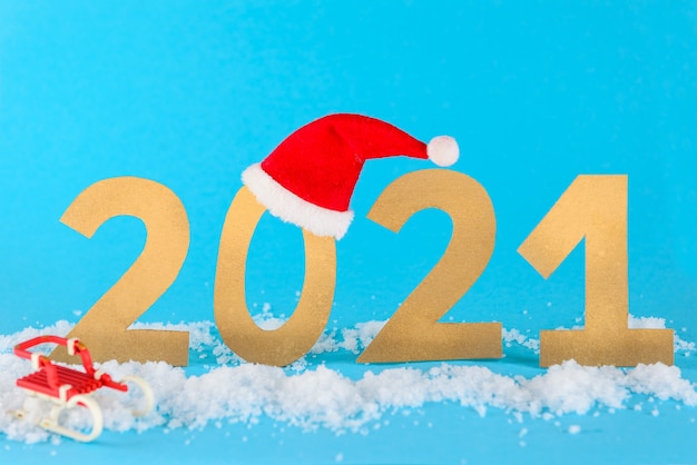 Natal de 2021, número na neve com trenós e chapéu sobre fundo azul.