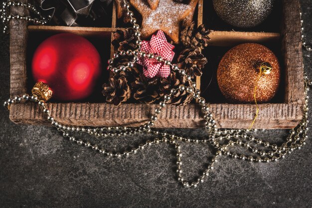 Natal, decoração de feriado de ano novo. Bolas de árvore de Natal, guirlanda, estrelas de gengibre, molde de biscoitos, arcos para presentes, cones de abeto em caixa de madeira na mesa de pedra preta, vista superior