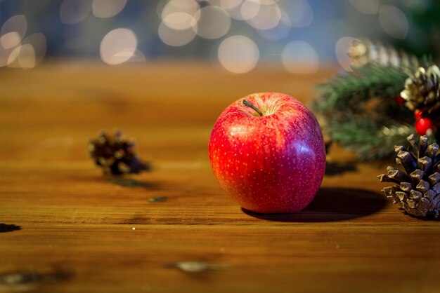 natal, decoração, feriados e conceito de ano novo - close-up de maçã vermelha com decoração de ramo de abeto na mesa de madeira