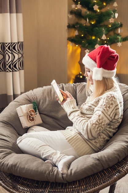 Natal e ano novo online. mulher com chapéu de Papai Noel e usando o smartphone.