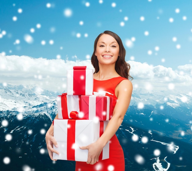 natal, feriados, celebração e conceito de pessoas - mulher sorridente de vestido vermelho com caixas de presente sobre fundo azul nevado