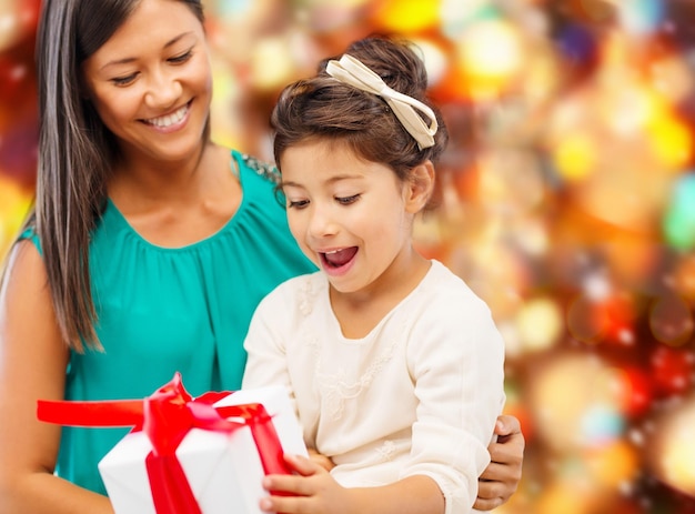 natal, feriados, celebração, família e conceito de pessoas - feliz mãe e garotinha com caixa de presente sobre fundo de luzes vermelhas