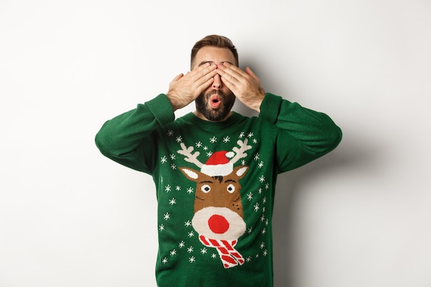 Natal, feriados e comemorações. Jovem feliz fechando os olhos e sorrindo, esperando o presente surpresa, em pé sobre um fundo branco